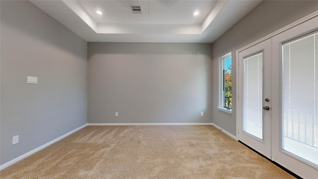 carpeted spare room with french doors and a raised ceiling