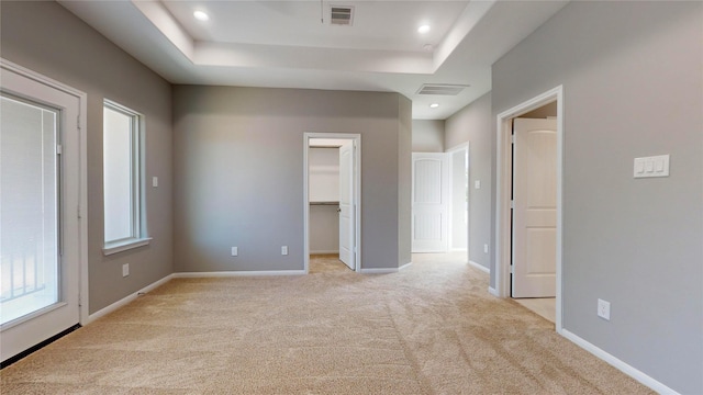 unfurnished bedroom with a spacious closet, light carpet, and a tray ceiling