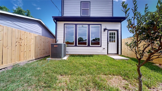 rear view of property with a fenced backyard, a lawn, and central AC