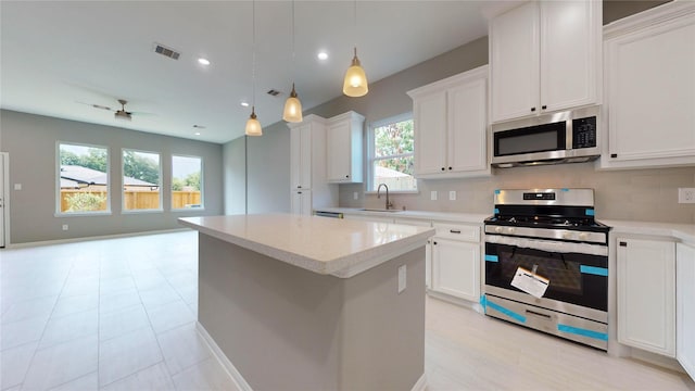 kitchen with white cabinets, appliances with stainless steel finishes, a kitchen island, and pendant lighting