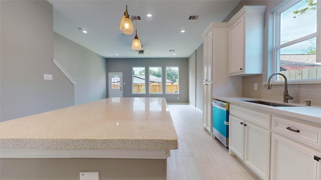 kitchen featuring light stone counters, sink, white cabinets, and decorative light fixtures