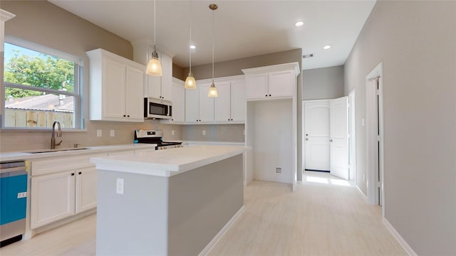 kitchen with a center island, pendant lighting, light countertops, appliances with stainless steel finishes, and a sink