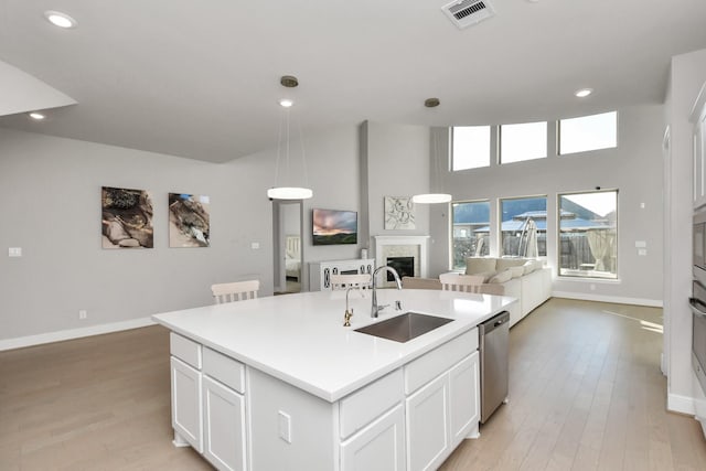 kitchen featuring a kitchen island with sink, sink, stainless steel dishwasher, light hardwood / wood-style floors, and white cabinetry