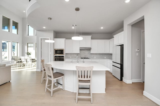 kitchen with white cabinetry, stainless steel appliances, backsplash, pendant lighting, and a kitchen island with sink