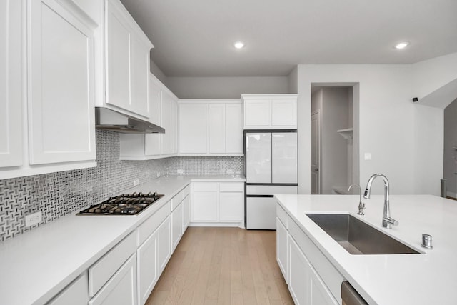 kitchen featuring sink, range hood, white fridge, stainless steel gas stovetop, and white cabinets