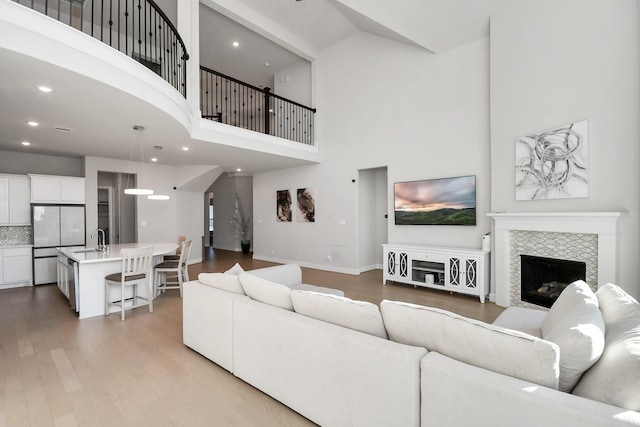 living room featuring a fireplace, sink, a high ceiling, and light hardwood / wood-style flooring