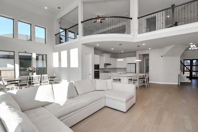 living room featuring a high ceiling, light wood-type flooring, ceiling fan, and sink