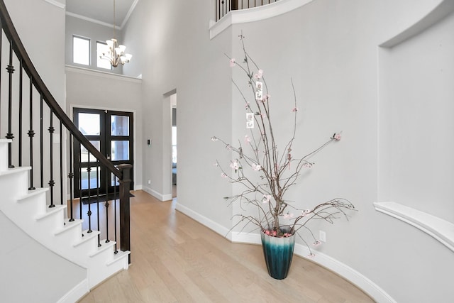 entryway with french doors, a towering ceiling, crown molding, hardwood / wood-style flooring, and a notable chandelier