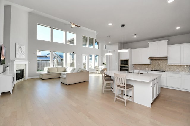 kitchen with backsplash, white cabinetry, oven, and an island with sink