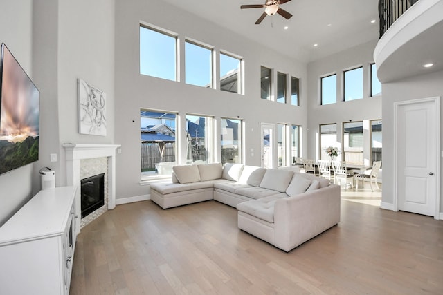 living room featuring ceiling fan, light hardwood / wood-style floors, and a towering ceiling