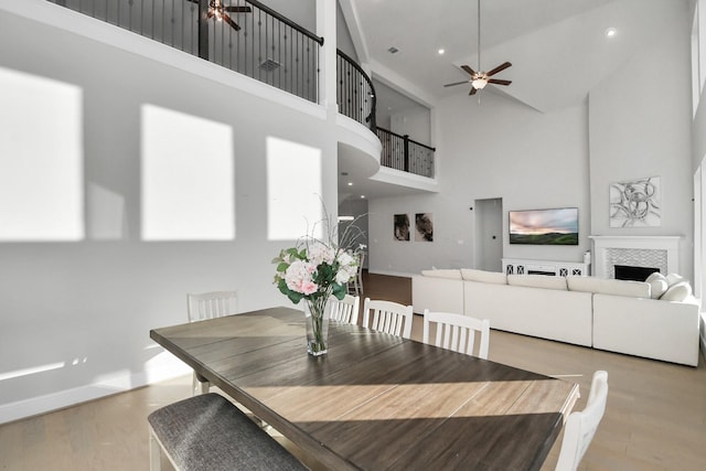 dining area with a tile fireplace, ceiling fan, light hardwood / wood-style flooring, and a high ceiling