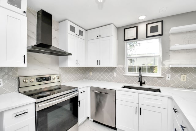 kitchen with appliances with stainless steel finishes, sink, white cabinetry, and wall chimney range hood