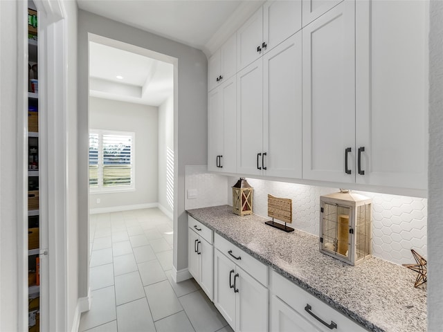 bar featuring tasteful backsplash, a tray ceiling, light tile patterned flooring, light stone counters, and white cabinetry