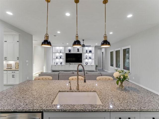 kitchen with light stone counters, sink, white cabinets, and pendant lighting