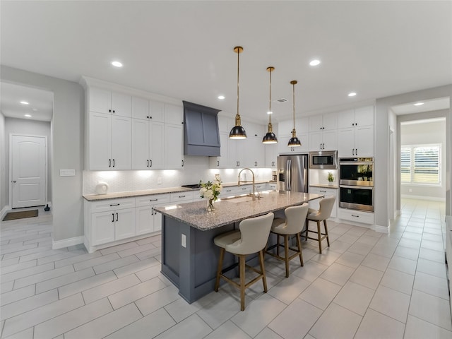 kitchen featuring a center island with sink, sink, light stone countertops, a kitchen bar, and stainless steel appliances