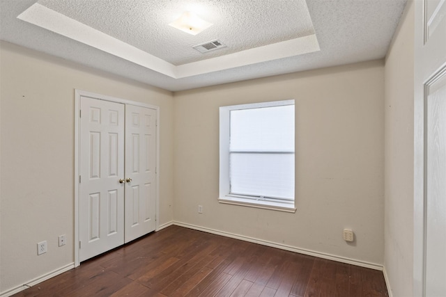 unfurnished bedroom with a tray ceiling, a closet, dark hardwood / wood-style flooring, and a textured ceiling