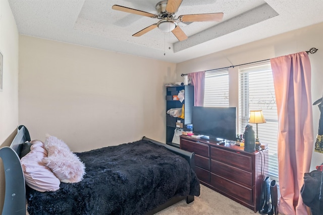 bedroom with a raised ceiling, ceiling fan, light carpet, and a textured ceiling