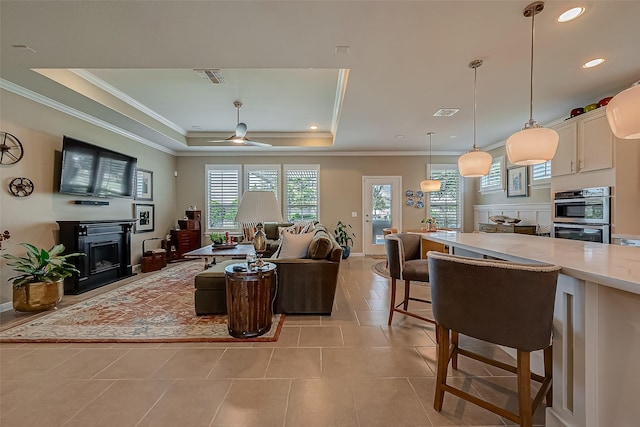 tiled living room with ceiling fan, a raised ceiling, and ornamental molding