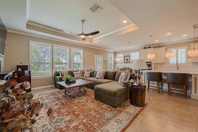 tiled living room featuring plenty of natural light, ceiling fan, a raised ceiling, and crown molding