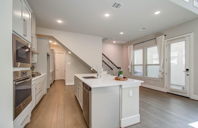 kitchen with appliances with stainless steel finishes, an island with sink, light hardwood / wood-style floors, and sink