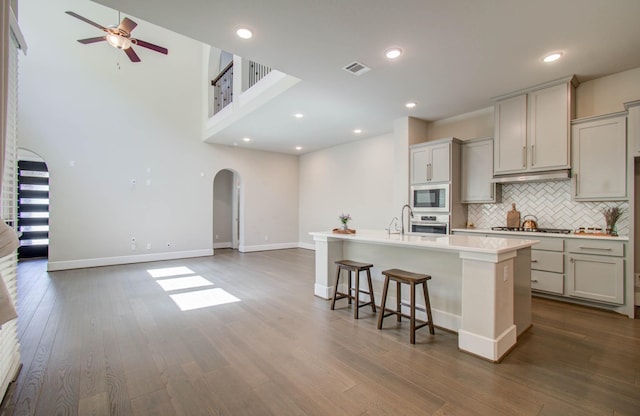 kitchen with gray cabinets, a kitchen island with sink, dark wood-type flooring, and appliances with stainless steel finishes