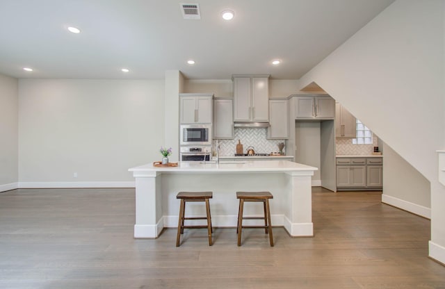 kitchen featuring a kitchen bar, light wood-type flooring, stainless steel appliances, a center island with sink, and gray cabinets