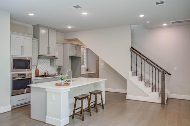 kitchen featuring sink, stainless steel appliances, light hardwood / wood-style floors, gray cabinets, and decorative backsplash