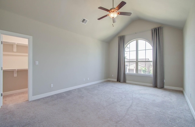 unfurnished bedroom featuring light carpet, vaulted ceiling, ceiling fan, a spacious closet, and a closet