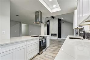 kitchen with electric stove, sink, wall chimney exhaust hood, light stone countertops, and white cabinetry