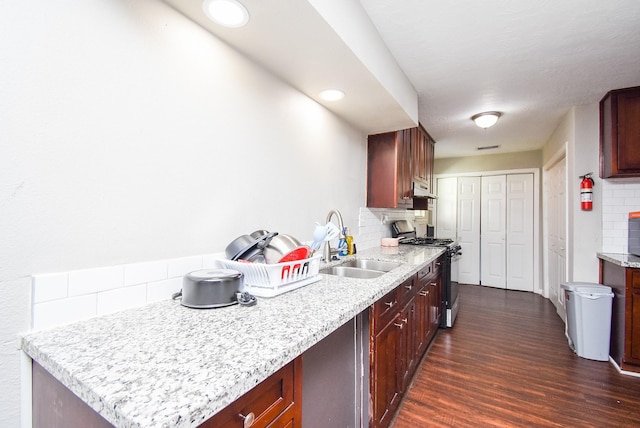 kitchen featuring dark wood-type flooring, sink, tasteful backsplash, and stainless steel gas range oven