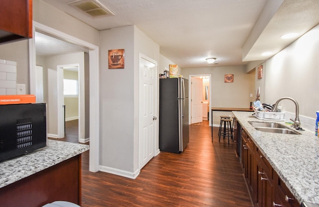 kitchen featuring light stone counters, sink, dark hardwood / wood-style flooring, and stainless steel refrigerator