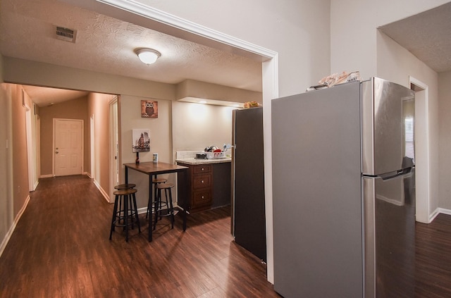 kitchen featuring stainless steel refrigerator, a breakfast bar, dark hardwood / wood-style floors, dark brown cabinetry, and a textured ceiling