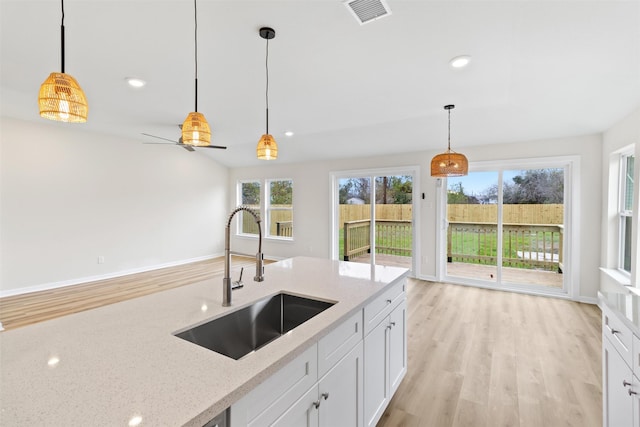 kitchen with light stone countertops, pendant lighting, white cabinetry, and sink