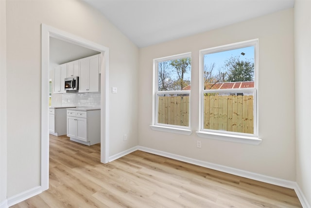 unfurnished dining area with light hardwood / wood-style floors and vaulted ceiling