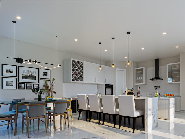 kitchen with a center island, wall chimney range hood, tasteful backsplash, black oven, and white cabinetry