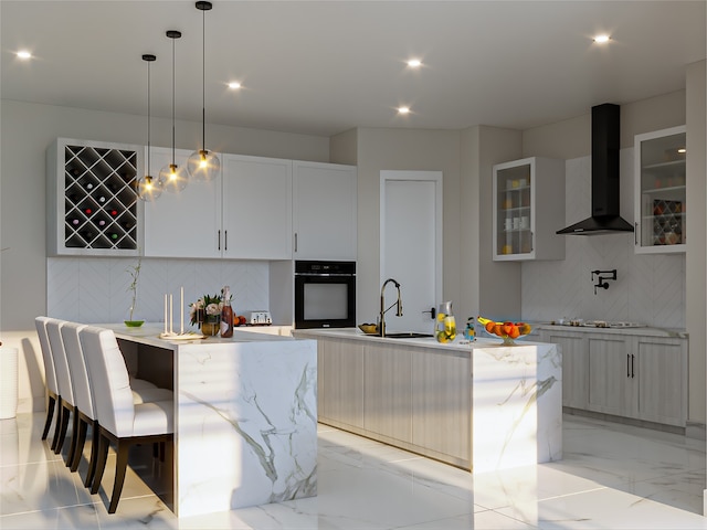 kitchen featuring black oven, white cabinetry, a center island with sink, and wall chimney exhaust hood