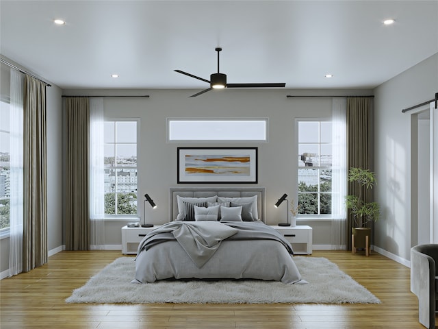 bedroom with a barn door, ceiling fan, and light hardwood / wood-style flooring