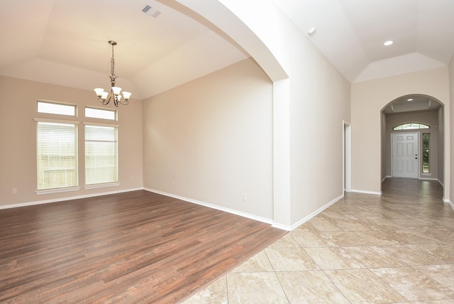 empty room featuring a raised ceiling, light hardwood / wood-style flooring, vaulted ceiling, and a notable chandelier