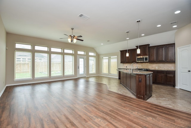 kitchen featuring dark brown cabinetry, ceiling fan, light stone counters, pendant lighting, and decorative backsplash