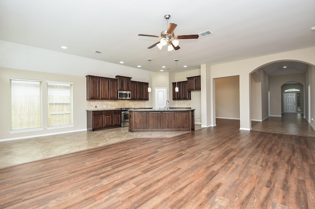 kitchen featuring appliances with stainless steel finishes, backsplash, dark brown cabinetry, hardwood / wood-style floors, and an island with sink