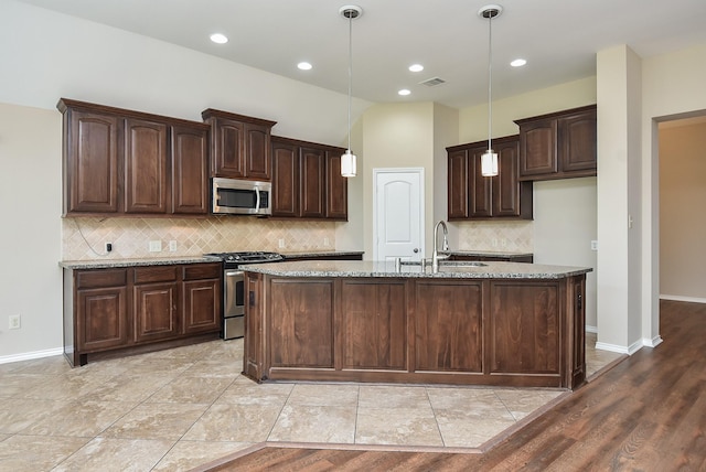 kitchen featuring a kitchen island with sink, sink, decorative light fixtures, and appliances with stainless steel finishes