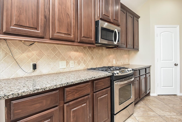 kitchen featuring light stone countertops, appliances with stainless steel finishes, backsplash, dark brown cabinetry, and light tile patterned flooring