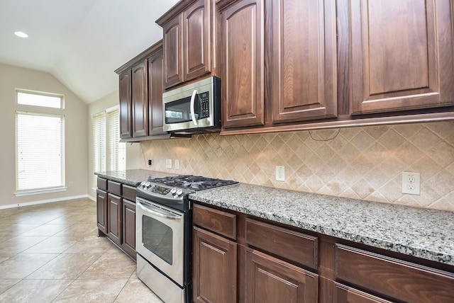 kitchen with vaulted ceiling, light tile patterned floors, light stone countertops, appliances with stainless steel finishes, and dark brown cabinetry