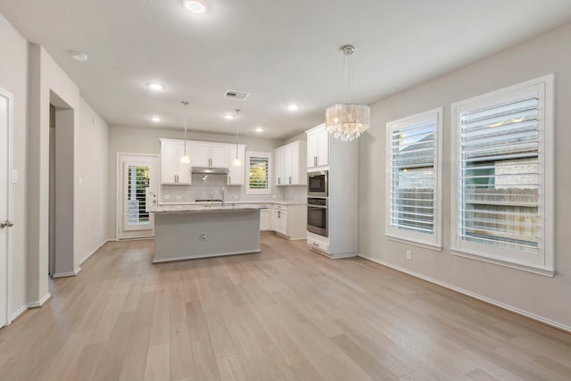 kitchen with built in microwave, pendant lighting, white cabinets, a center island, and oven