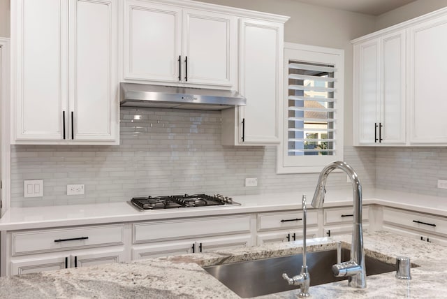 kitchen featuring sink, light stone counters, backsplash, stainless steel gas stovetop, and white cabinets