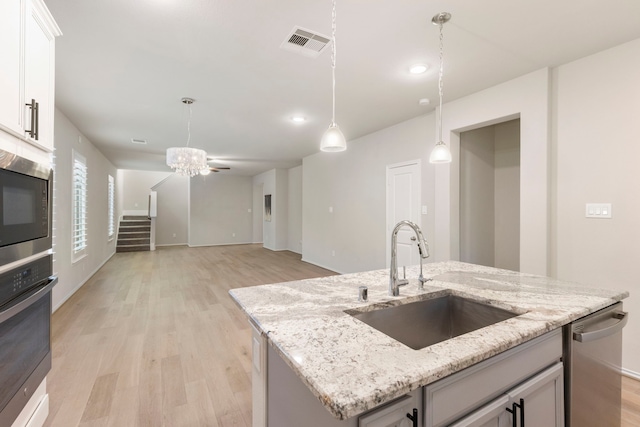 kitchen with white cabinetry, sink, stainless steel appliances, light stone counters, and an island with sink