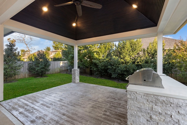 wooden terrace with an outdoor kitchen, area for grilling, ceiling fan, and a lawn