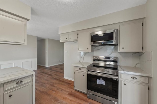 kitchen with light stone countertops, hardwood / wood-style floors, a textured ceiling, and stainless steel appliances