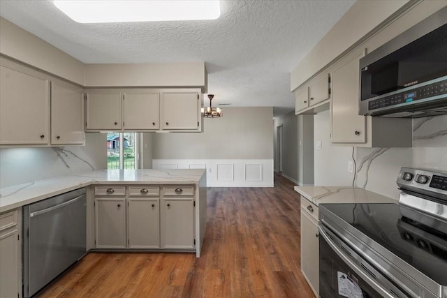 kitchen featuring kitchen peninsula, appliances with stainless steel finishes, light stone counters, a textured ceiling, and a chandelier