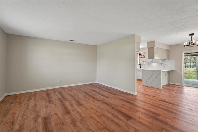 unfurnished living room with a textured ceiling, light hardwood / wood-style floors, and an inviting chandelier